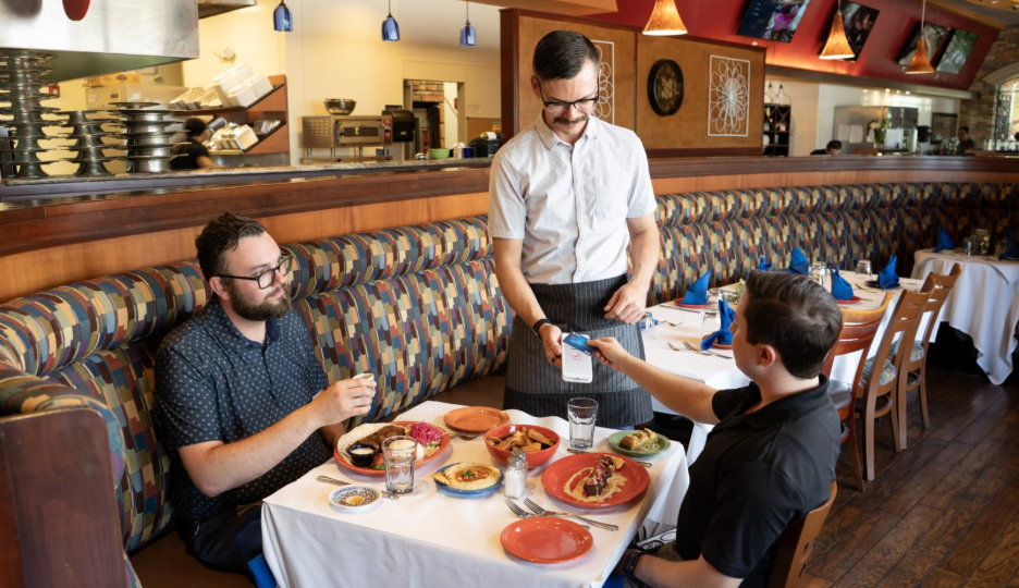 Customers paying for their meal at their restaurant table using a credit card.