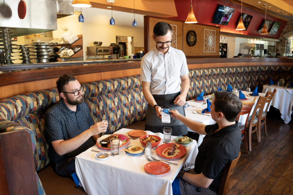 Customers paying for their meal at their restaurant table using a credit card.
