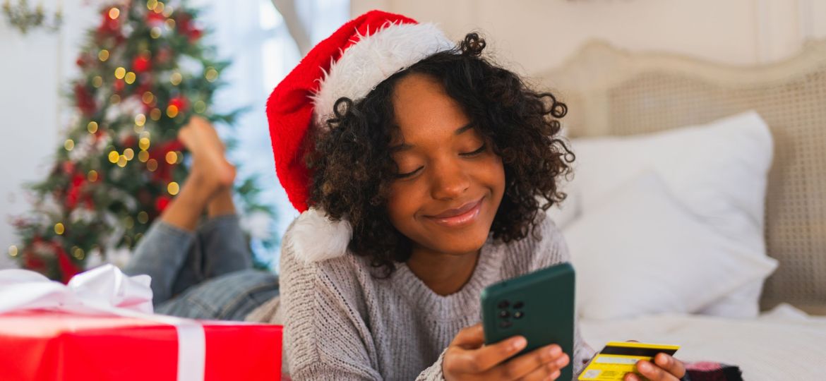 A smiling woman holding a gift card and her phone on Christmas morning.