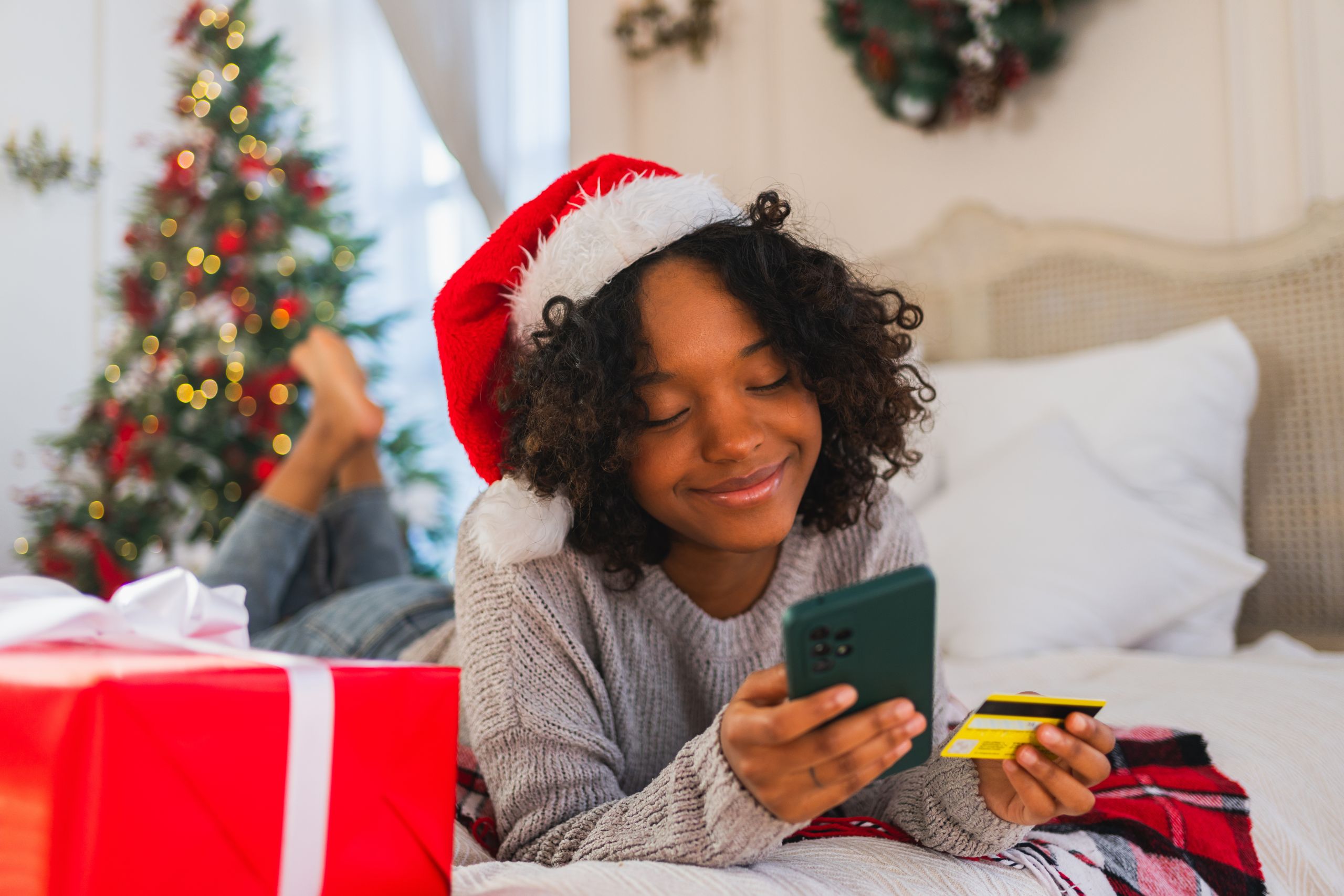 A smiling woman holding a gift card and her phone on Christmas morning.